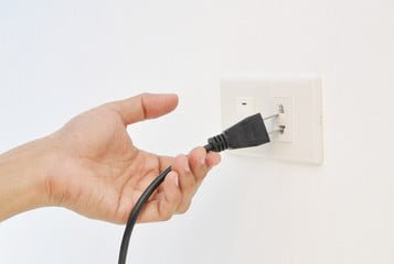 A hand is plugging a power cord into a wall outlet.