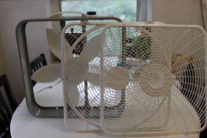 Three fans sitting on a table in a kitchen.