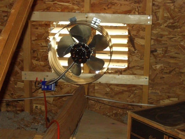 A ceiling fan in an attic with a wooden frame.