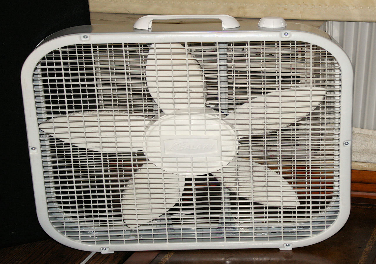 A white fan sitting on a wooden floor.