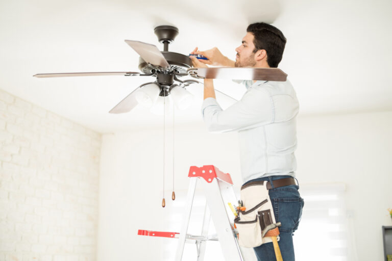 A man installing a ceiling fan on a ladder.