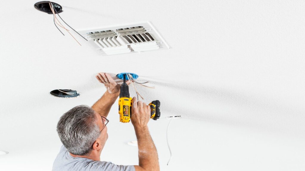 A man installing a ceiling fan in a room.